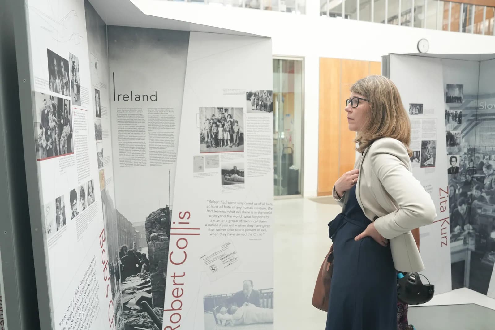A woman wearing glasses and a light-colored jacket stands in profile, looking at a museum exhibit panel about Ireland.